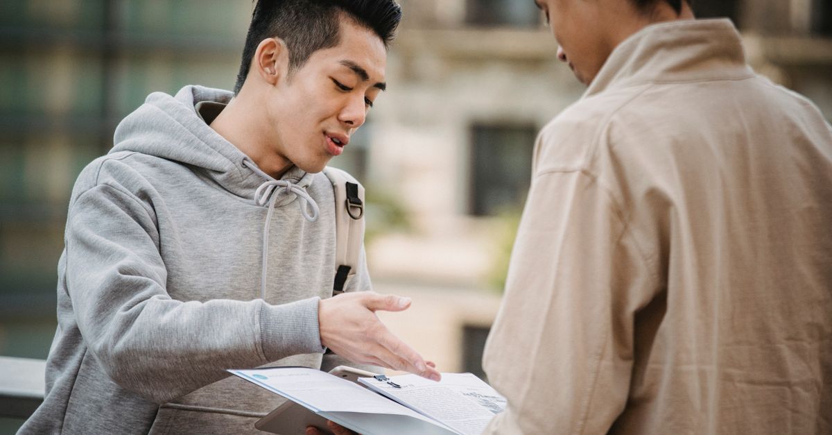 Concentrated multiracial friends talking about exam and discussing information about subjects on blurred background of street